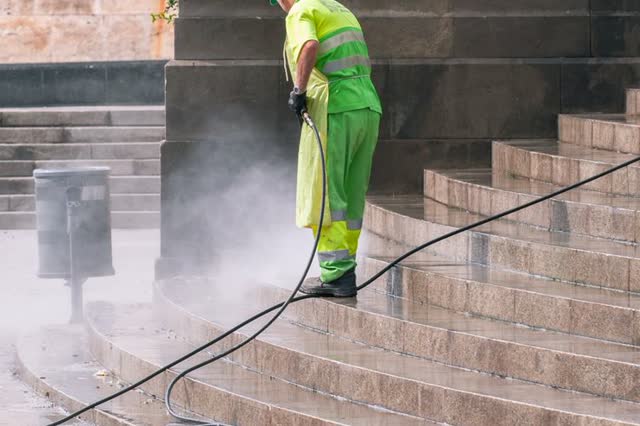 A worker pressure-washing stone steps